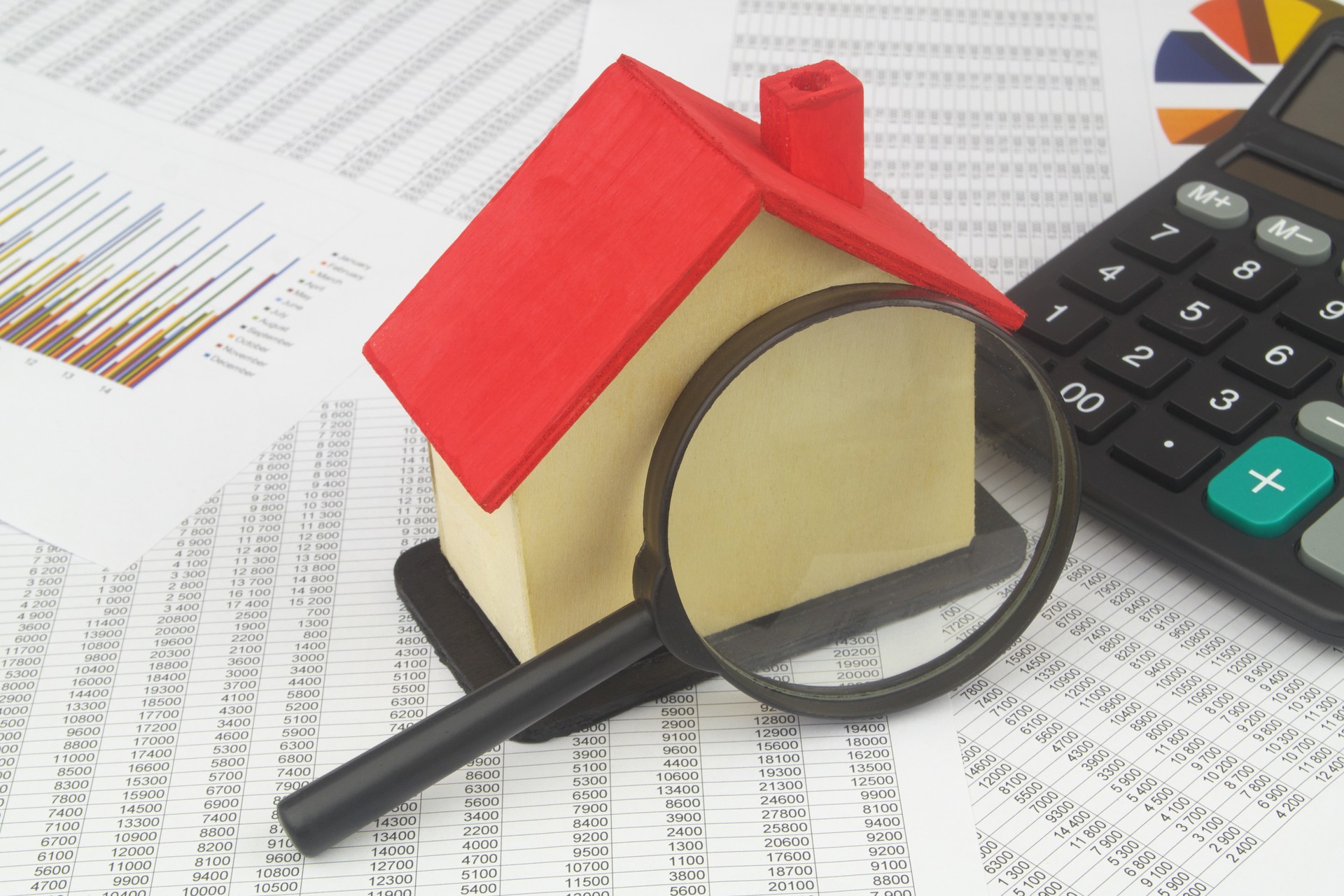 House model with magnifying glass and calculator on financial documents.